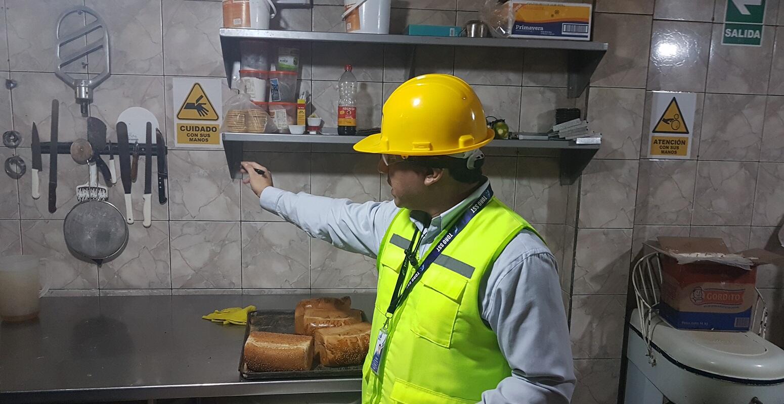 Sistema de aviso para riesgos laborales: Un trabajador de SST midiendo la altura de una señal de obligación de casco en una obra de construcción en Arequipa.